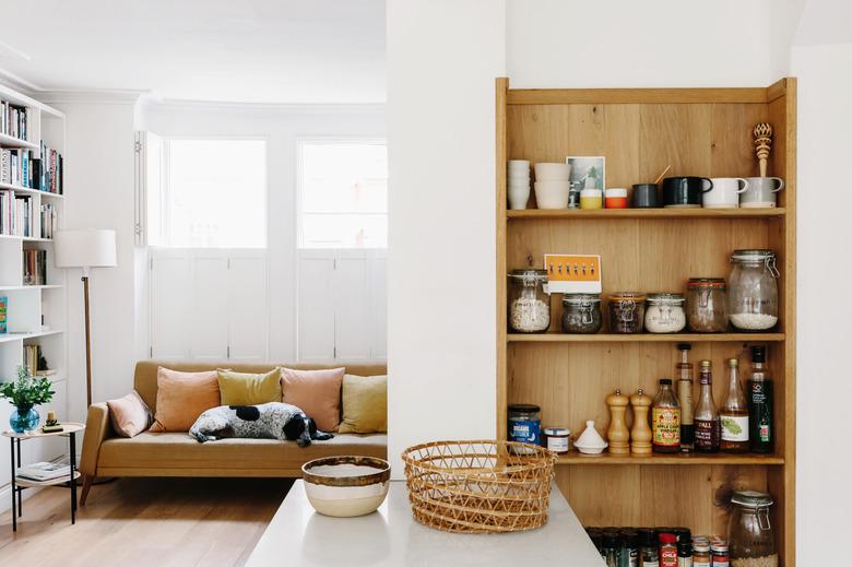 living room with yellow couch, dog, bookshelves, and vertical kitchen cabinetry