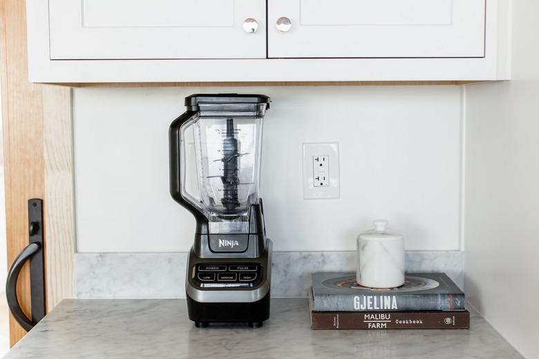 Black Ninja blender on a marble countertop. Next to the blender, two cookbooks – Gjelina and Malibu Farm – are stacked on top of each other. A marble container is on top of them.