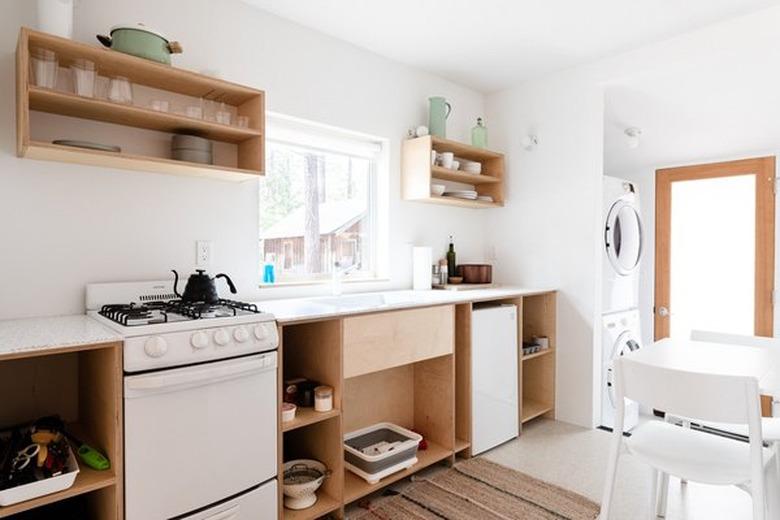 Kitchen with small stove, plywood shelves, small fridge, white table and chairs. stove size