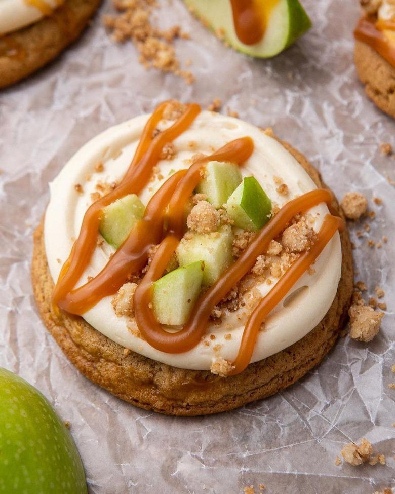 A caramel apple cookie with white frosting, chunks of green apple pieces, and a caramel drizzle.