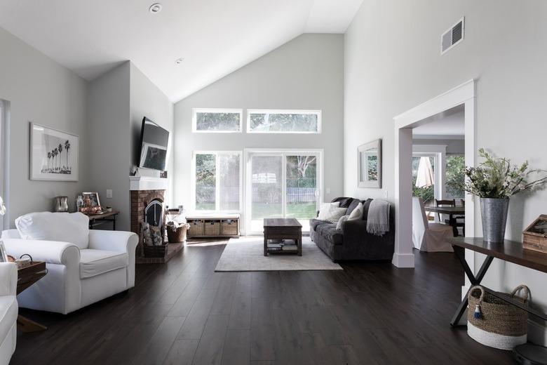 A living room with light gray walls, white millwork and wood floors. Furnished with gray and white furniture, and wood tables.