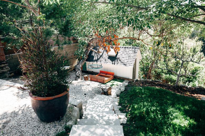 A sloped backyard with concrete steps, stone landscape edging, a large black pot with an evergreen tree