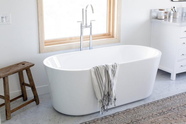 A freestanding garden tub in a white bathroom next to a wooden stool