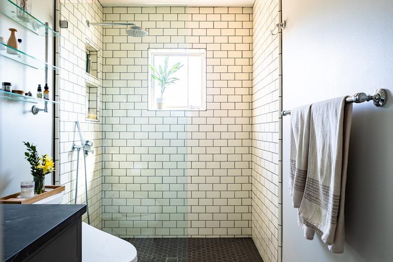 A white tiled shower with glass doors in a bathroom with black floors