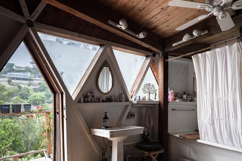 pedestal sink, shower/tub combo in front of triangular windows with view of the outside