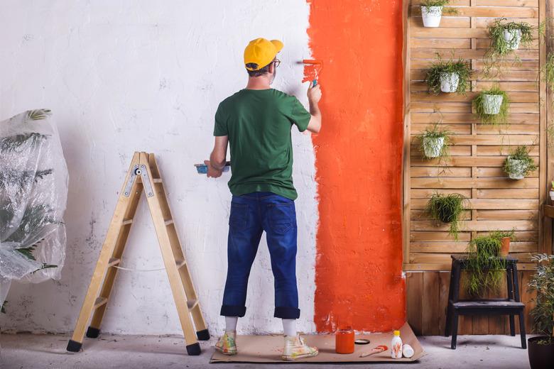 Rear view of man painting a wall orange in his garden terrace.