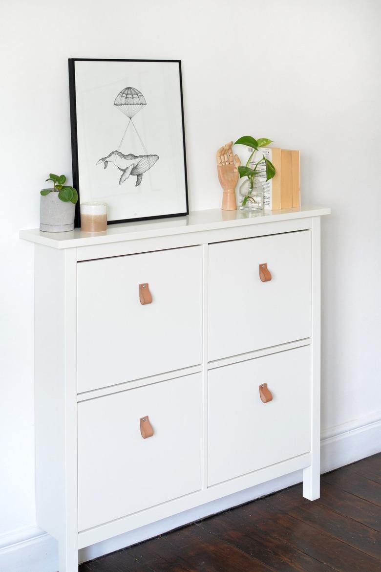 White dresser with leather pull handles on drawers with art and plants