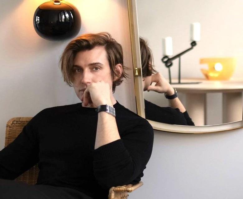 Jeremiah Brent wearing all black and leaning into his hand. He's sitting in a chair in front of a mirror.