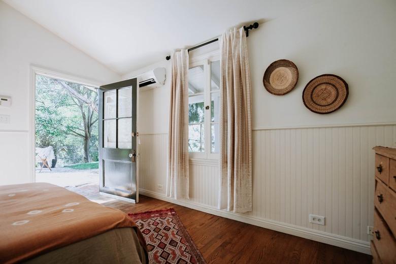 Bedroom with sloped ceiling, wood floors, green casement door, dark wood floor, beige curtained window, and woven textile decor