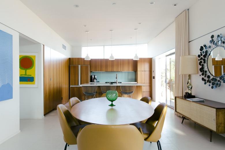 a dining area full of mid-century style, including mustard-yellow chairs, a low console, and a mirror with a starburst frame