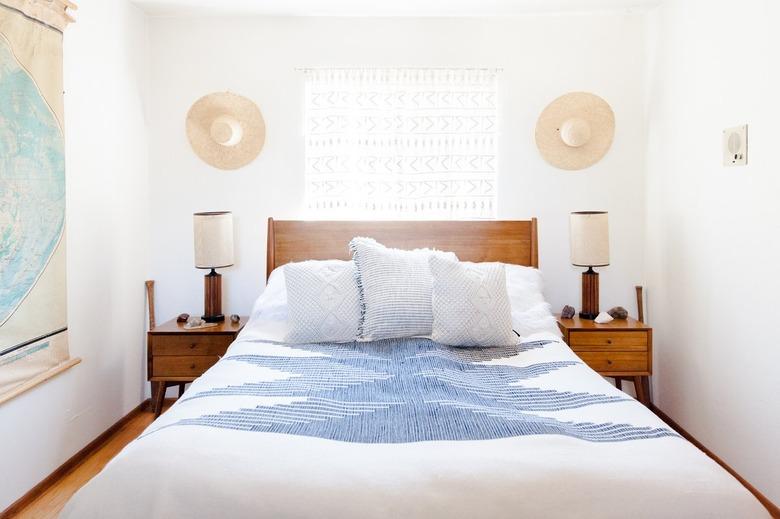 A white bedroom with a sheer lace curtain hanging in the window