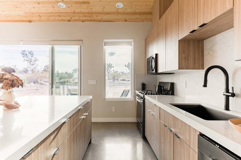 Minimalist kitchen with wood counters, black sink faucet, drop-in sink, wood cabinets, and ceiling.