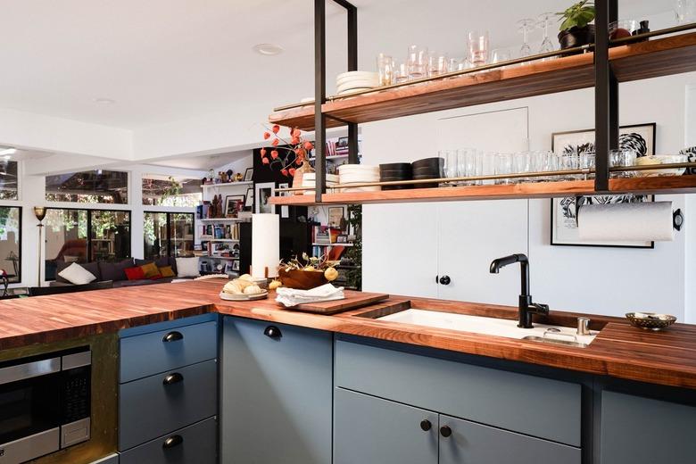 Blue kitchen cabinets with wood floating shelves and a butcher block countertop