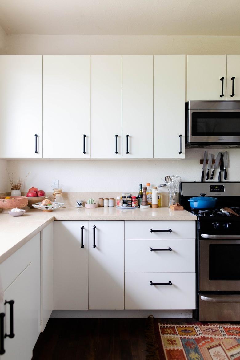 Minimalist kitchen with white cabinets and beige countertops and colorful rug