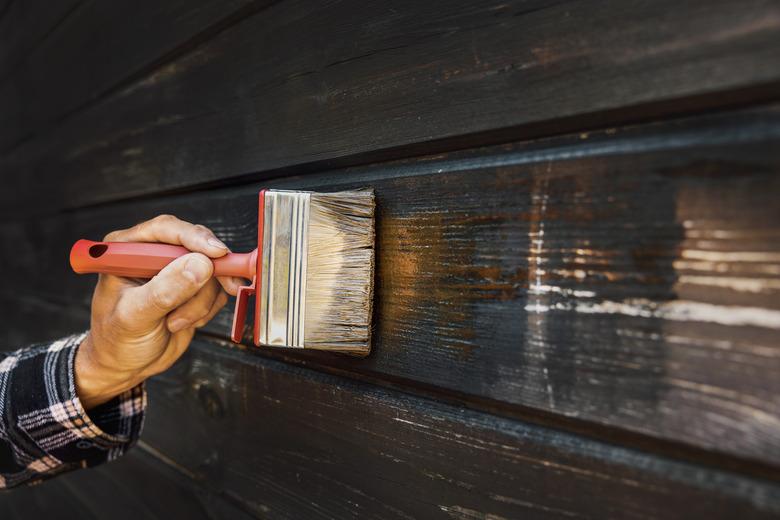 hand with brush restore paint of old wooden house exterior wall