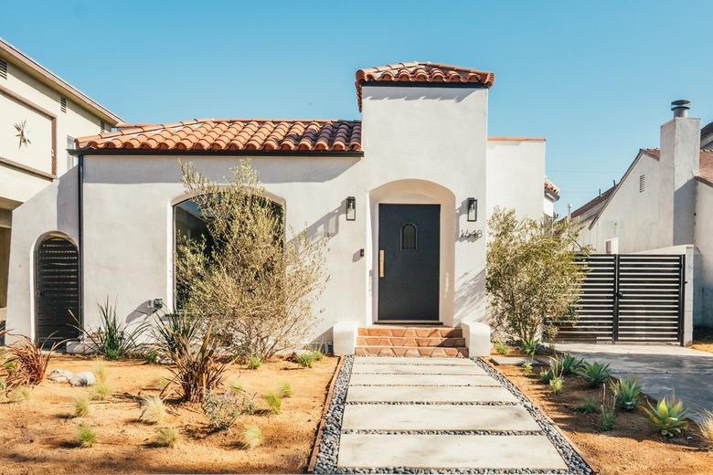 Gravel and concrete step path leading to Spanish style white house with terracotta front steps and tile roof