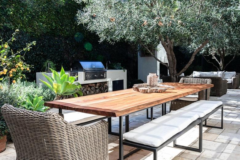 A wood table with benches and wicker chairs on a patio