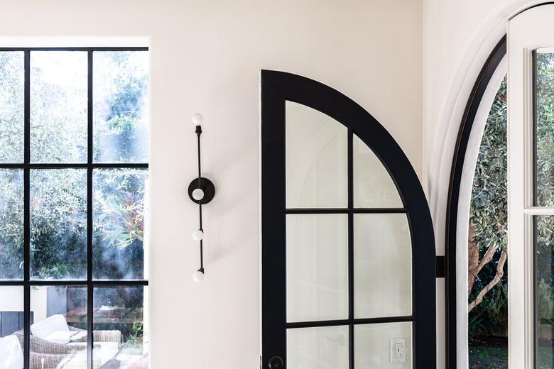 A black French door in a room with white walls and a wall sconce