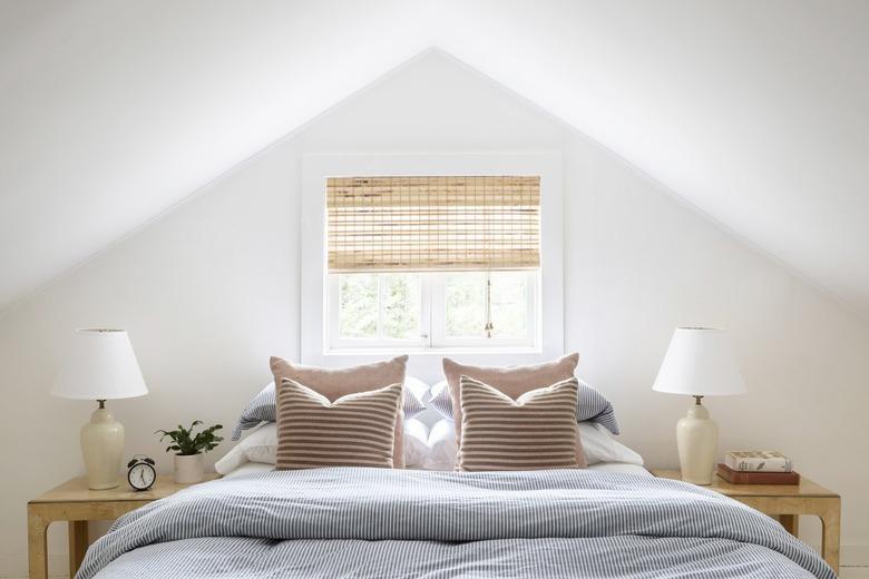 a bed with a blue pinstripe comforter and two matching blonde-wood end tables under a steeply sloping roof