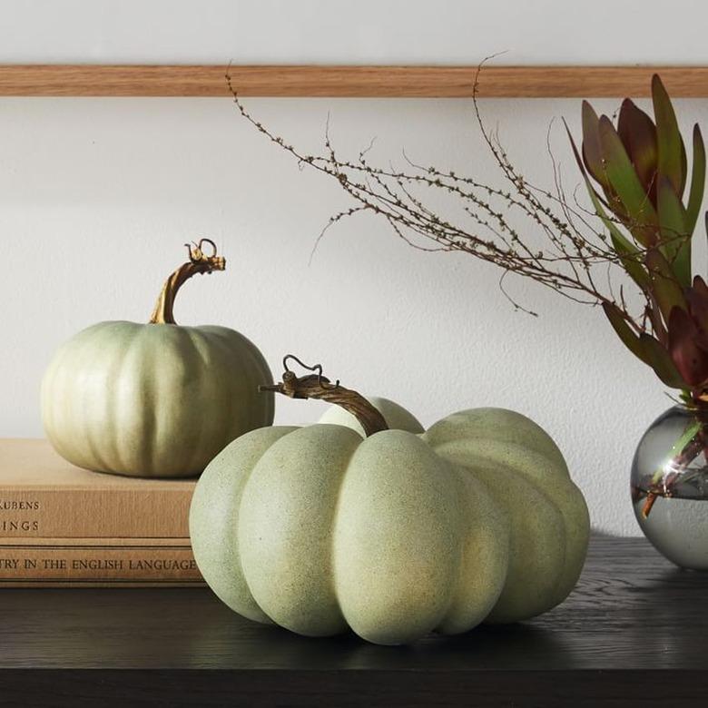 A sage large artificial pumpkin on a dark wood surface.