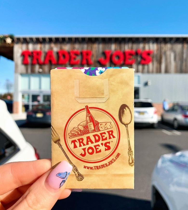 Hand holding up a Trader Joe's gift card in front of a store with the logo seen in the back.