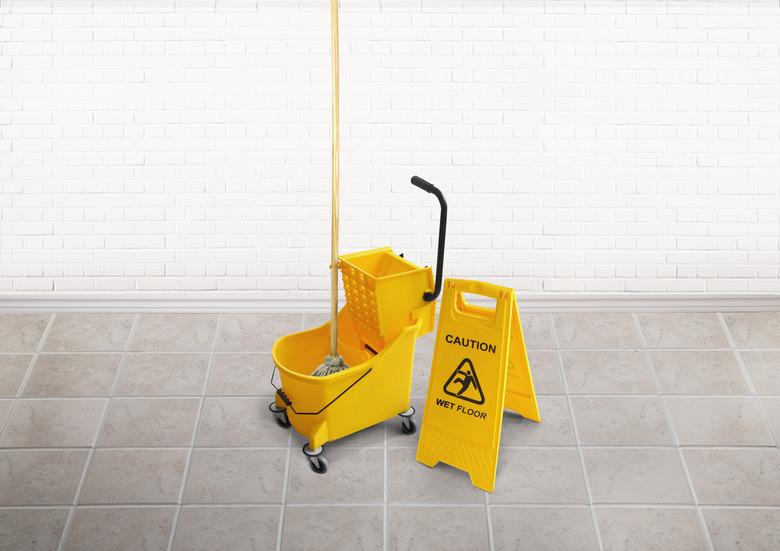 Cleaning bucket with mop and a wet floor slippery sign in an empty room