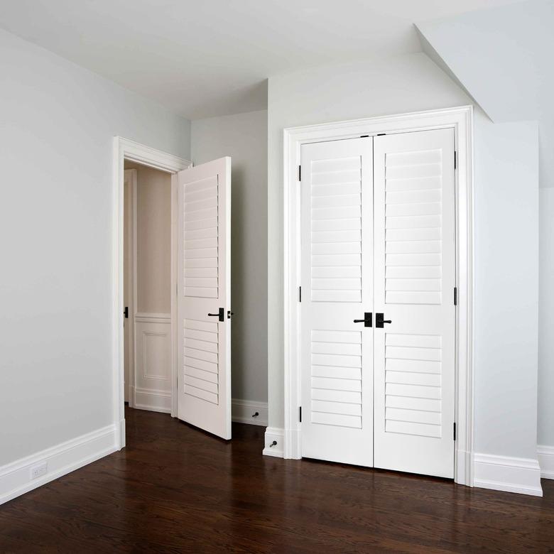 A white louvered closet door in a bedroom