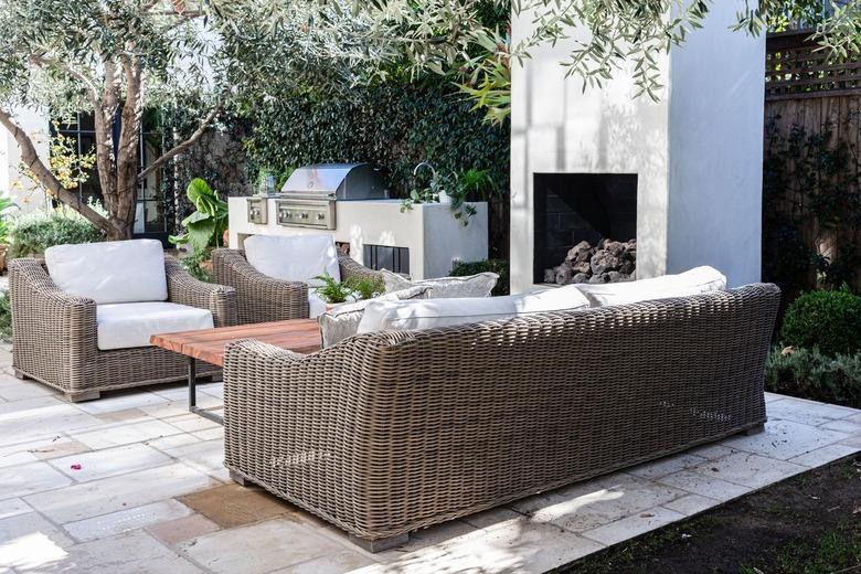 Wicker patio seating and outdoor fireplace on a patio surrounded by trees