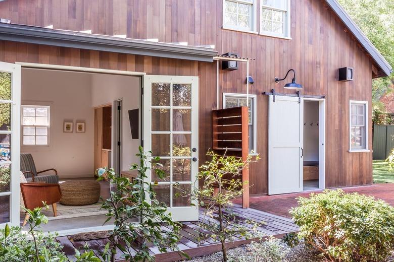 A dark wood barn with white French doors, an outdoor shower, and a wood deck.