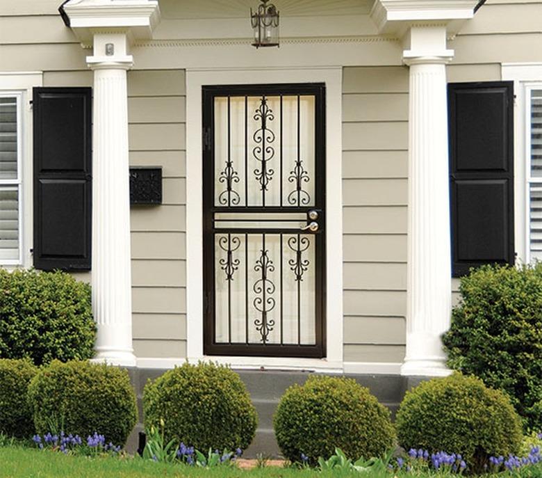 A black iron security screen door on a house with two white columns and ivory siding