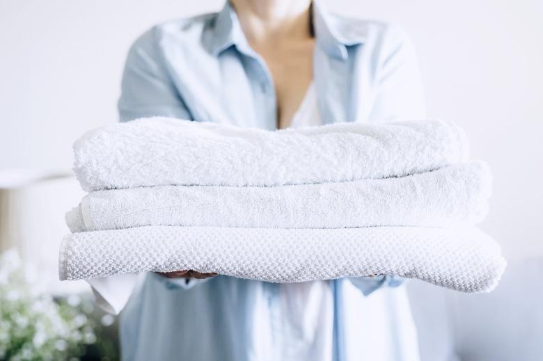 Figure holding three white folded towels in an outdoor daytime setting