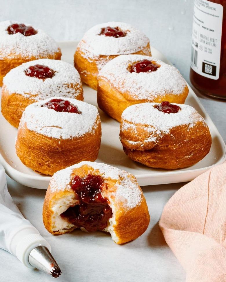 Six vegan jelly donuts on a white tray with one in the front with a bite taken out of it.