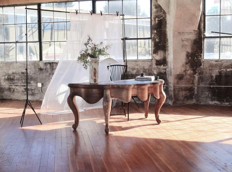 An antique French light wood writing desk in an industrial space with lots of windows.