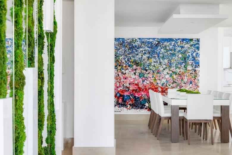 A contemporary Miami dining room with polished travertine floors, cool white walls, and wall art in saturated hues