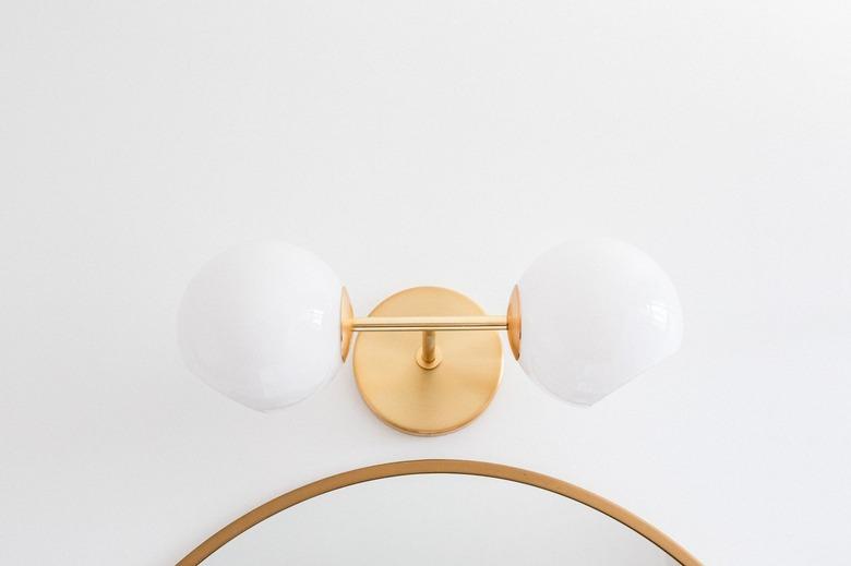 Gold wall sconce with globes over a mirror