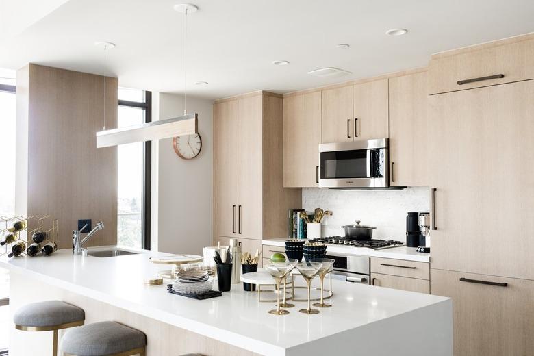 Light wood cabinet kitchen with a bar pendant light, white kitchen island, martini set, hexagonal wine rack, and bar stools.