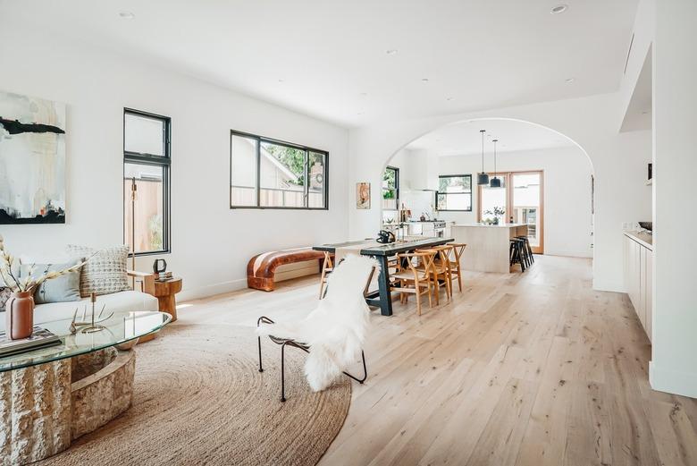 Glass and coffee table on a round fiber rug by an accent chair with a sheep throw. Light wood flooring and and arch room dividers.