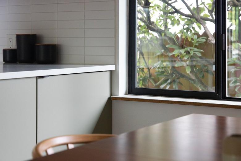 Gray kitchen cabinets and white backsplash, by a window.