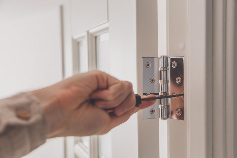 Man remove the door. Twists self-tapping screw with a screwdriver. Stainless door hinges on a white door