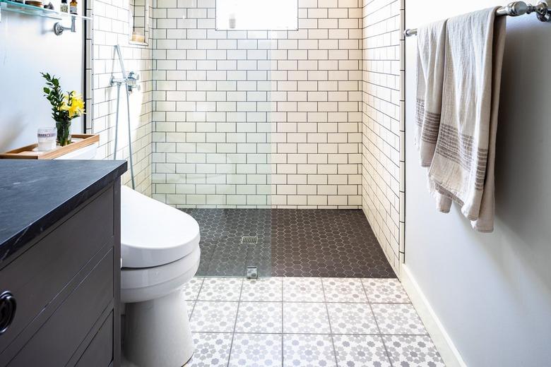 A white tiled bathroom with a glass door shower and black-gray accents