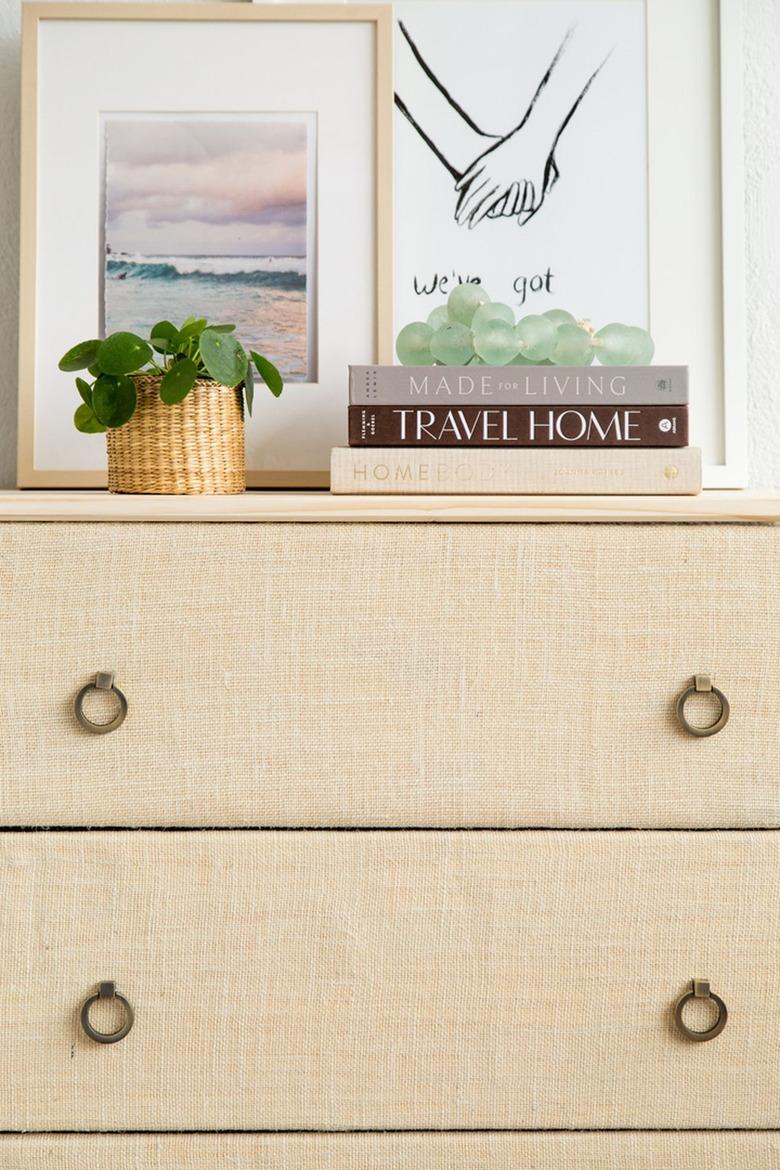 IKEA Tarva cabinet with round drawer handles, covered in burlap, with art, books and a Pilea plant