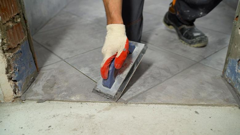 Man grouting the joints between the tiles with a sponge. The hand of man holding a rubber float and filling joints with grout. The worker rubs the seams on the floor, ceramic tiles.