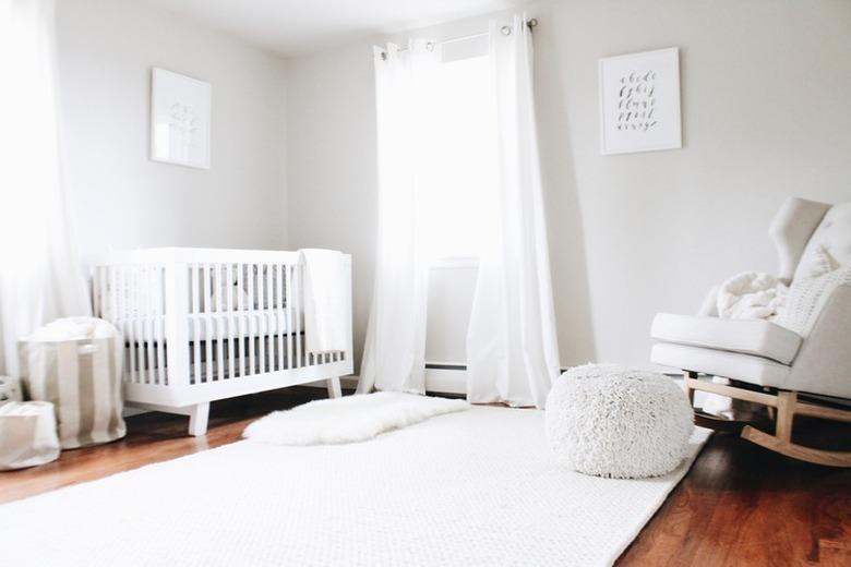 minimal white nursery with upholstered rocker and pouf