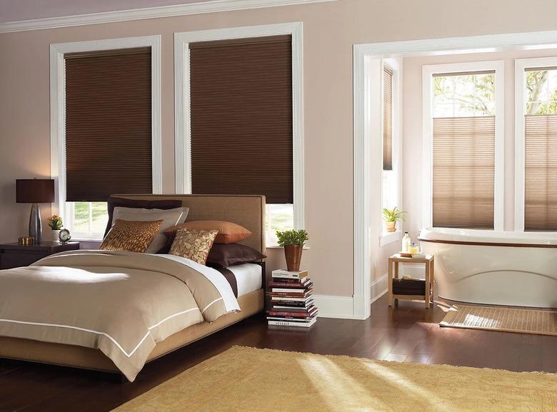 A primary bedroom with a freestanding tub and brown insulated cellular shades