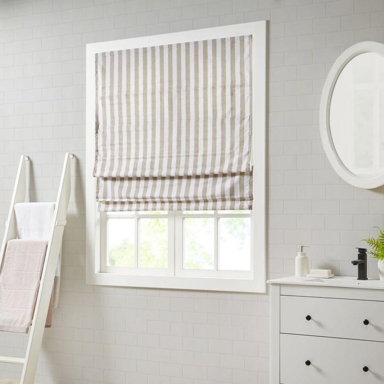 A vertical striped Roman shade in a white bedroom