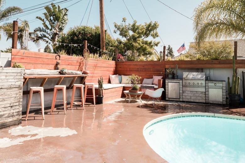 Outdoor patio with a swimming pool, and a fence with a built-in wood bench and side table.