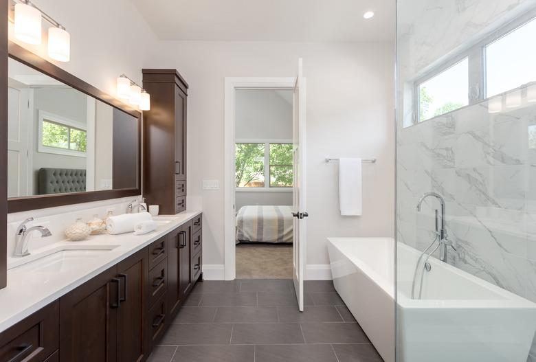 master bathroom interior in luxury home large mirror, shower, and bathtub. Includes dark hardwood cabinets and tile floor. View of bedroom