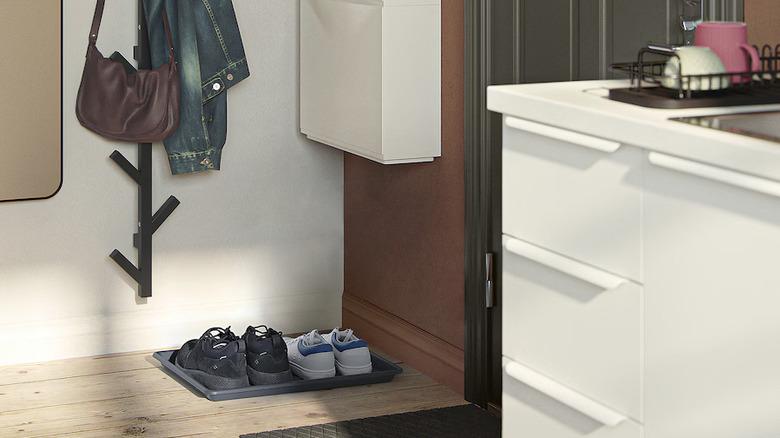 small corner entryway off the kitchen with a small IKEA BAGGMUCK shoe tray on the ground holding two pairs of shoes, a wall-mounted coatrack, and wall-mounted storage cabinet