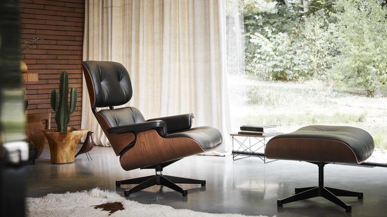 living room with a replica of the black leather and wood Eames lounge and ottoman in front of an exposed brick wall and floor-to-ceiling window with white drapery