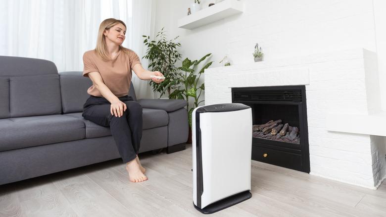 woman using remote control on air purifying unit in living room